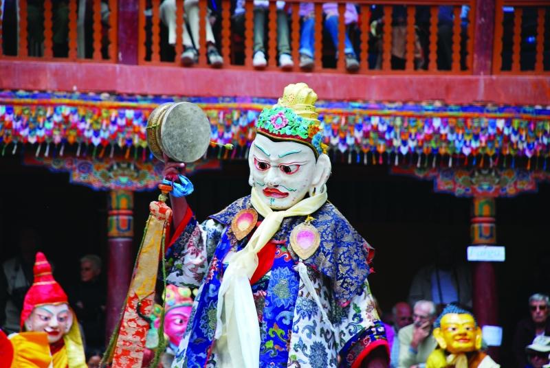 Guru Pema Gyalpo hóa thân của đức Liên Hoa Sinh, mang mặt nạ trắng, trên hai tay ngài là trống và chuông kim cương.
